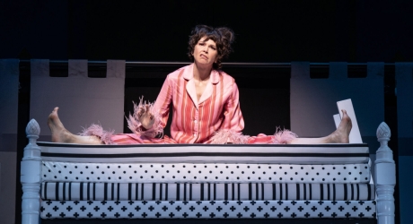 Sutton Foster in fluffy pink pajamas sitting splay-legged on a stack of mattresses